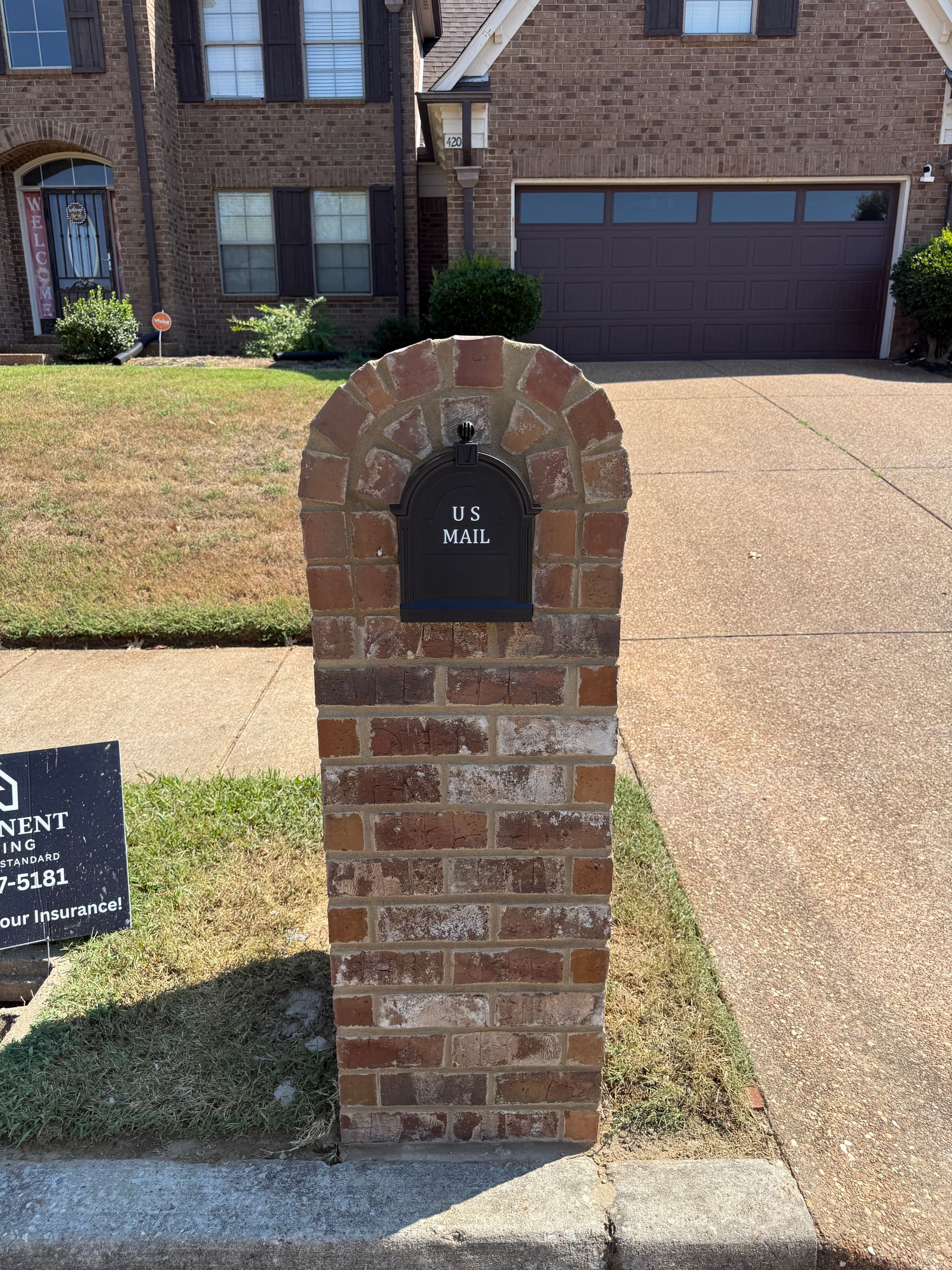 Brick mailbox column with a rowlock arch over a set black mailbox, beside a driveway