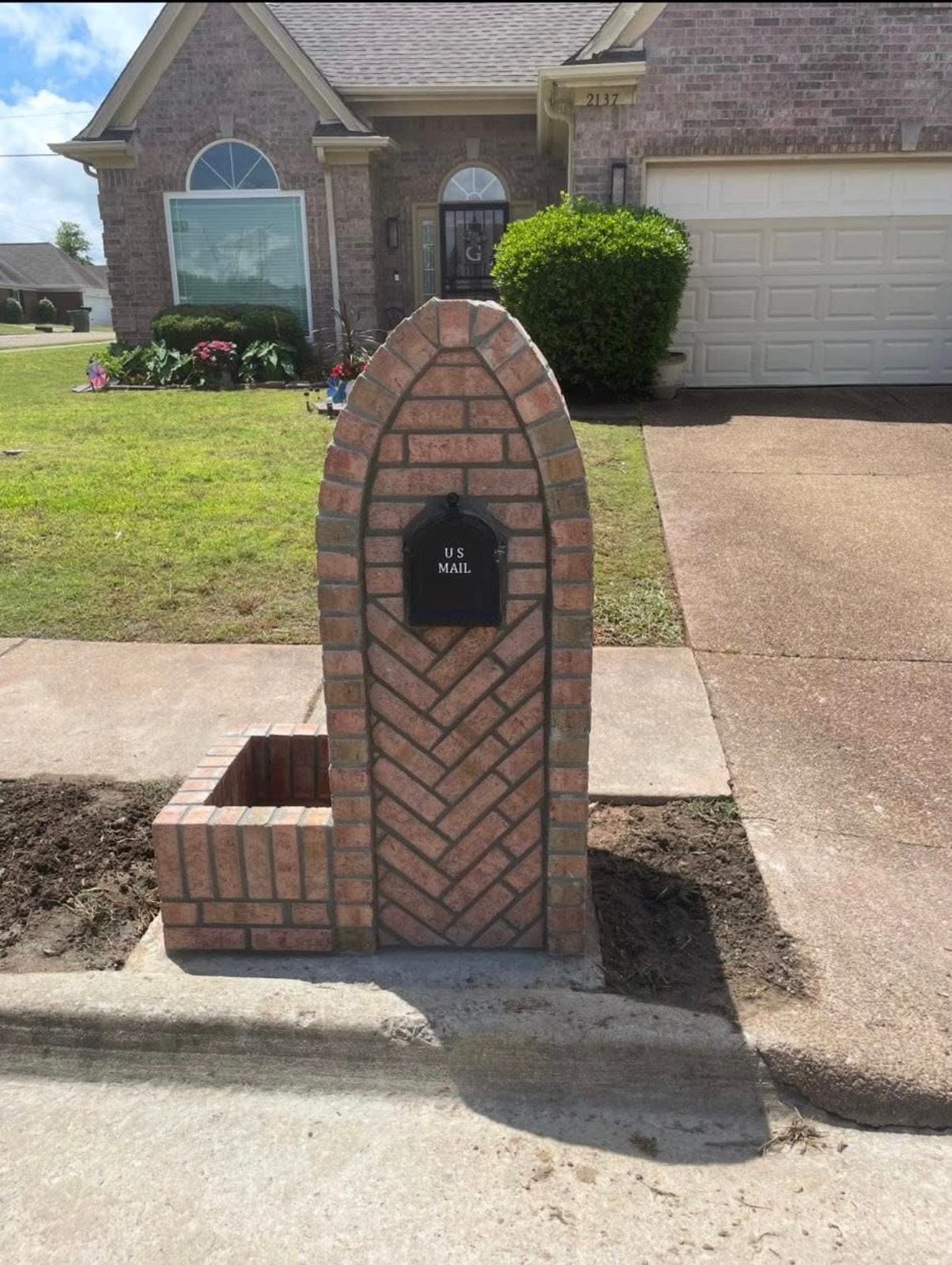 Arched brick mailbox with a herringbone infill panel and a low planter box