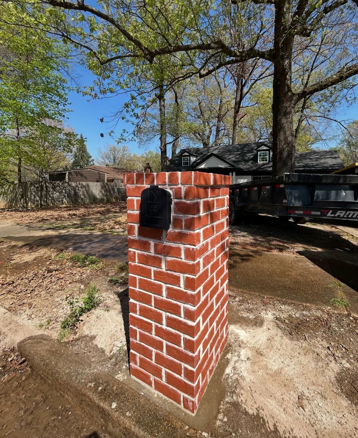 Red brick mailbox column with a capped top, standing on a cleared site