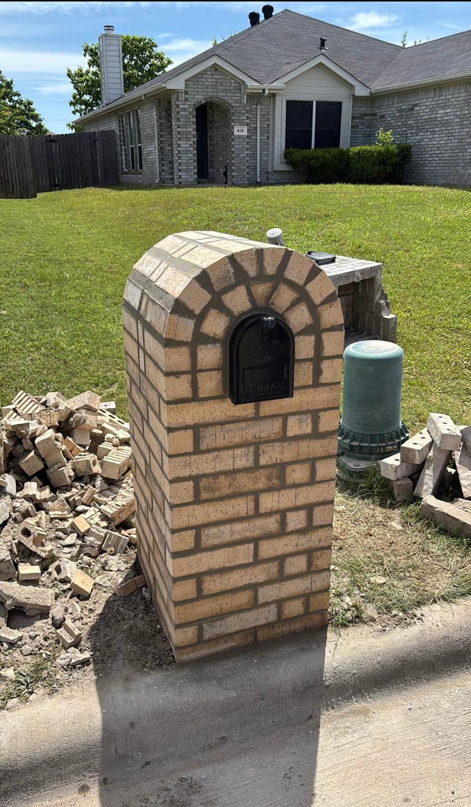 Arched brick mailbox with the site still uncleared around it
