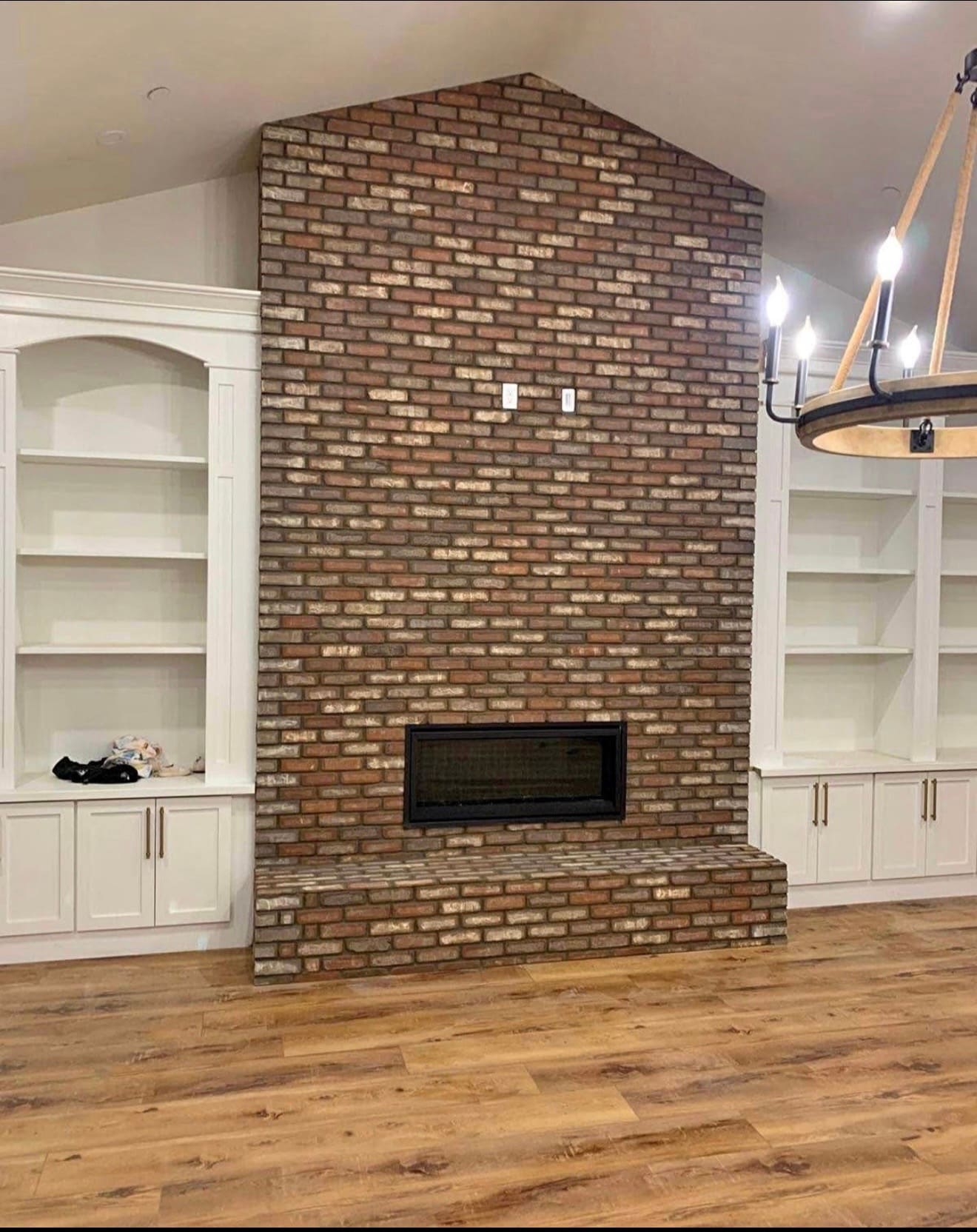 Full-height brick fireplace wall with a raised hearth and a linear firebox, between built-in shelves